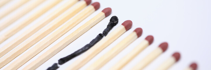 Close-up view of one wooden burnt match among many new whole. Conceptual image of non-renewable energy. Burn out syndrome and stress concept. Isolated on white background