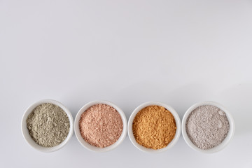 Set of different cosmetic clay mud powders on white background