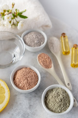 Set of different cosmetic clay mud powders on white background. Ingredients for homemade facial and body mask or scrub and fresh sprig of flowering cherry . Spa and bodycare concept.