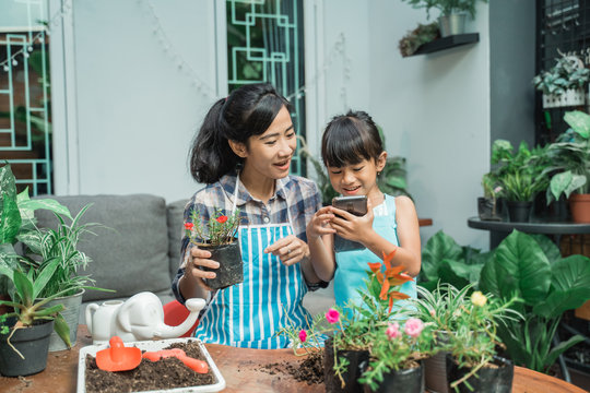 happy kid and mother gardening at home and using smartphone technology to advanced the technique