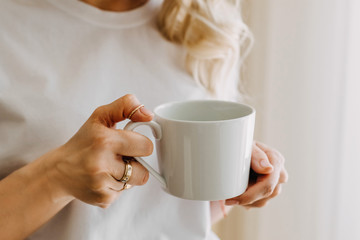 Close-up of a woman with blonde hair, holding a big white cup of coffee or tea.