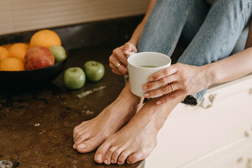 Close-up of a woman sitting in the kitchen, drinking green matcha tea from a white cup.