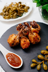 Fried chicken legs in breadcrumbs, next to red sauce. Food on a black plate.
