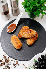 Fried pork cutlets in breadcrumbs, next to red sauce. Food on a black plate.