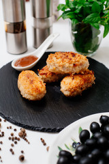Fried pork cutlets in breadcrumbs, next to red sauce. Food on a black plate.