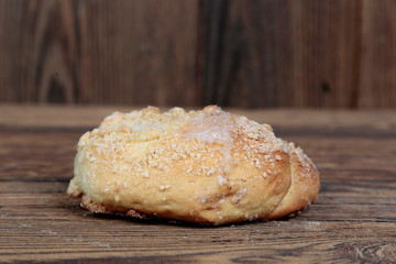 Side view, closeup of a fresh, homemade bread roll with sprinkles on a wooden, brown, rustic table.