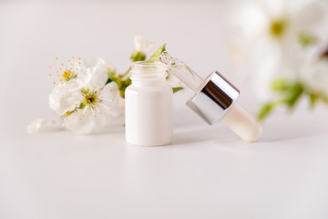 Obraz na płótnie Canvas White cosmetic skincare dropper bottle packaging cherry blossoms flowers on white background