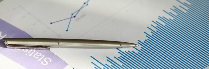 Close-up of analysis graphics on table with silver pen. Important documentation with colourful charts and graphs. Finance report accounting statistics business concept