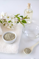 Ceramic bowl with green clay powder on white background. Ingredients for homemade facial and body mask or scrub and fresh sprig of flowering cherry . Spa and bodycare concept.