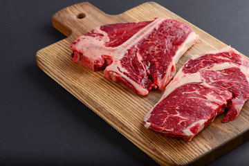 Fresh raw beef T-bone steak on wooden cutting board, top view. Porterhouse steak served over black background.