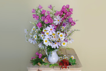Still life with bells and daisies in a vase and berries on a light background.Summer bouquet on the table.