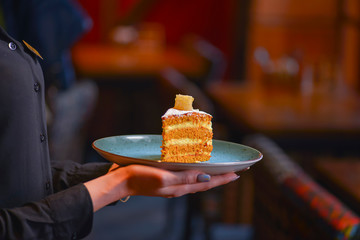 Waiter in black uniform, shirt, bringing the ordered dessert and in a cafe or restaurant.