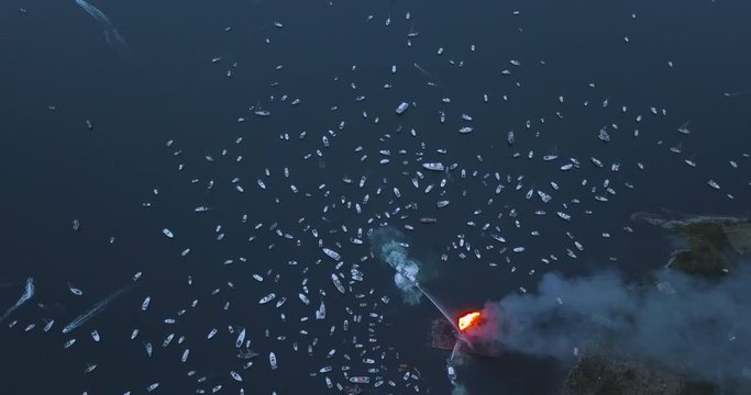 Unique revealing, high altitude, top down aerial footage of small motor boats and sail boats gathering around and witnessing the biggest bonfire event on Earth at Alesund, Norway at dusk.