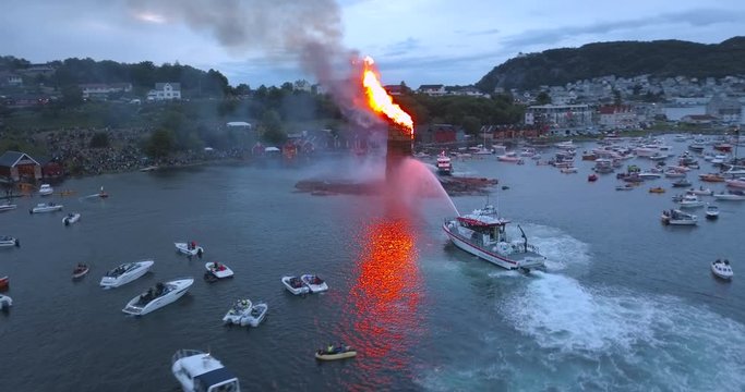 Unbelievably beautiful, cinematic, low level, forward flying aerial footage that reveals the biggest bonfire event on Earth and the small boats gathering around it near Alesund, Norway at dusk.