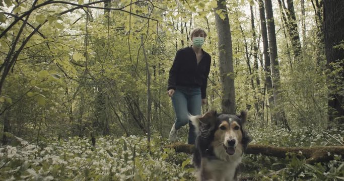 Woman give her female dog a sign to run free and take off face mask walking smiling on a forest trail in nature park on a post coronavirus staycation travel