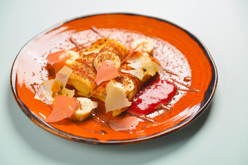 Banana pancake or crepe, with maple syrup and powdered sugar served on a orange brown plate over blue mint background.