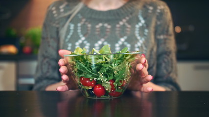 Crop view of Young woman preferring salad. Attractive young woman choosing to eat healthy salad for breakfast while sitting at table in stylish kitchen.