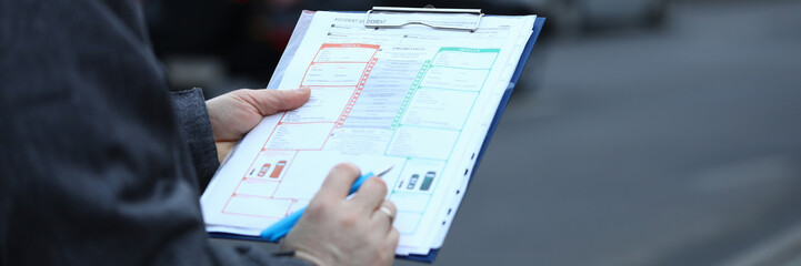 Close-up of male hands holding clipboard with documentations and writing down something. Accident statement document used after car crash. Road risk and incident concept