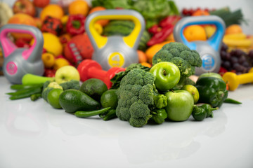 Fitness concept. Healthy nutrition: fruits and vegetables. Equipment for fitness exercises: weighing machine and dumbells. White background.