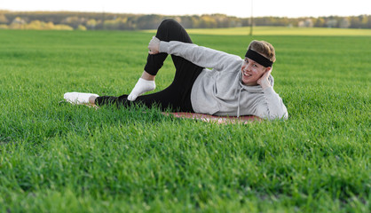 young man doing sports exercises in green field and looking at camera
