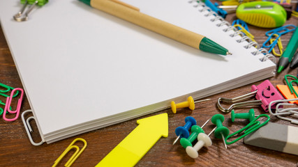 Different tools used at an office. School stationery on brown wooden table: multi-colored pencils, paper clips, chips, smiles binder clips. Education or knowledge