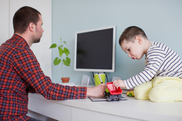 Working from home with kids. Young father is trying to work while his toddler son is distracting him