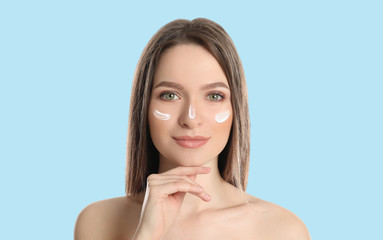 Young woman with sun protection cream on face against light blue background