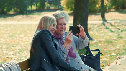 Zoom shot of young and old women making selfie on smartphone in autumn time in a beautiful autumn...