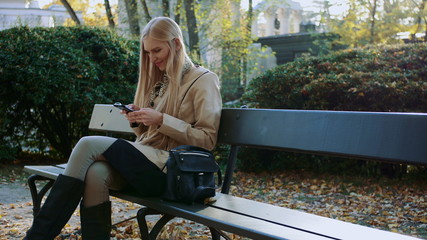 Fototapeta premium Girl communicates in a smartphone in a city park on a bench.