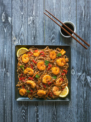 Asian food udon noodles with fried shrimps, sesame and pepper close-up on a plate on the wooden table.