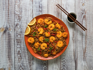 Asian food udon noodles with fried shrimps, sesame and pepper close-up on a plate on the wooden table