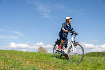 Fototapeta na wymiar Querfeldein mit dem E-Bike durch den Frühling, Frau genießt Fahrrad fahren in der Natur.