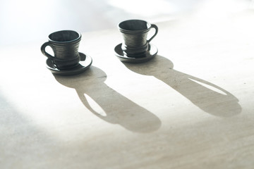 Two Coffee clay black cups on table with bright backlight which draws long cup shadows. Coffee for couple in modern kitchen concept.