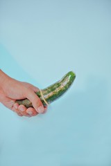 Hand firmly gripping cucumber with condom with bright colorful background. 