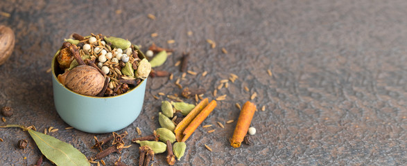Mix of different spices black and white peppercorns, cloves, cinnamon, mace, cardamom, cumin. Spice blend of ground spices in metal bowl on large concrete background for banner.Copy space
