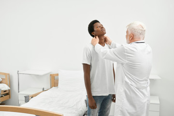 Fototapeta premium Eldery doctor examinating throat of african patient.