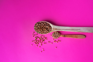 Wooden spoon of roasted buckwheat on buckwheat groat jar background, gluten free ancient grain for healthy diet, selective focus. Coronavirus food supplies. on a pink magenta background. top view.