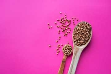 Wooden spoon of roasted buckwheat on buckwheat groat jar background, gluten free ancient grain for healthy diet, selective focus. Coronavirus food supplies. on a pink magenta background. top view.