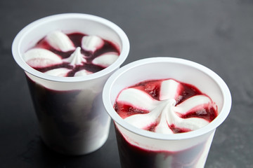 ice cream in a white plastic cups on black background, frozen sweet fruit dessert on dark stone table
