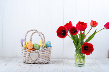 Multi-colored Easter eggs in a basket on a white wooden background
