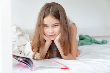 school concept. little girl with book lying on bed