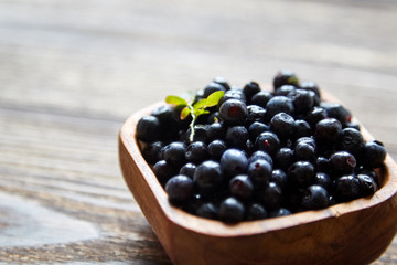 Blueberries (Bilberries) with green leaf into a bowl on brown wooden background, many fresh dark blue berries