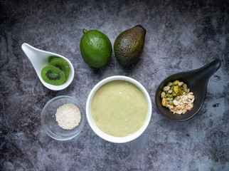 Avocado Smoothie Breakfast bowl (avocado , banana , almond milk, Natural flavored yogurt) topped with Dry Kiwi Slice Welding, Pistachio, chopped  nuts and sesame seeds. Top View. Vegan Food