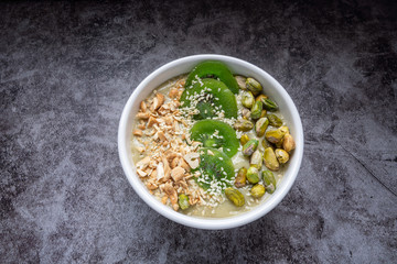 Avocado Smoothie Breakfast bowl (avocado , banana , almond milk, Natural flavored yogurt) topped with Dry Kiwi Slice Welding, Pistachio, chopped  nuts and sesame seeds. Top View. Vegan Food