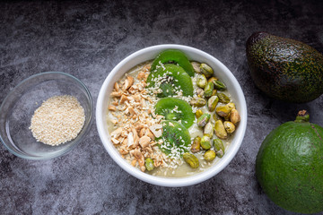 Avocado Smoothie Breakfast bowl (avocado , banana , almond milk, Natural flavored yogurt) topped with Dry Kiwi Slice Welding, Pistachio, chopped  nuts and sesame seeds. Top View. Vegan Food