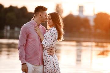 beautiful couple in love are standing and hugging near the lake on sunset. Lovely happy couple having fun near outdoors. happy holiday concept