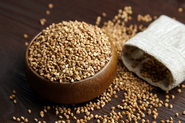 Buckwheat groats (hulled seeds) in bowl and burlap bag on wooden table