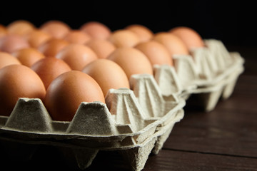 Egg tray on wooden background. Brown chicken eggs in recycled cardboard package on table