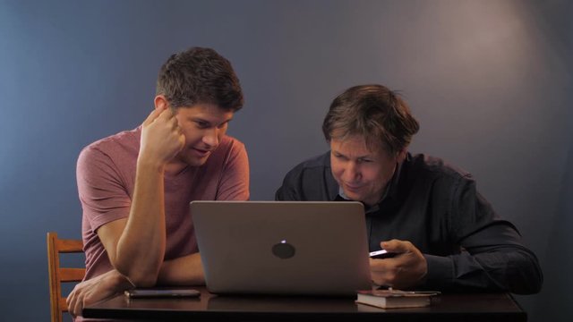 young man teaches senior father to input computer password from phone at table in room slow motion. Concept technology education