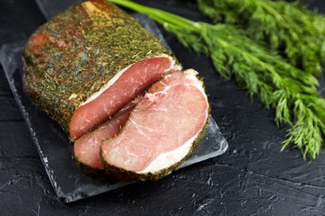 Gerky pork with spices, fresh green dill, slate cutting board on black stone table. Polendwitz is a jerky tenderloin